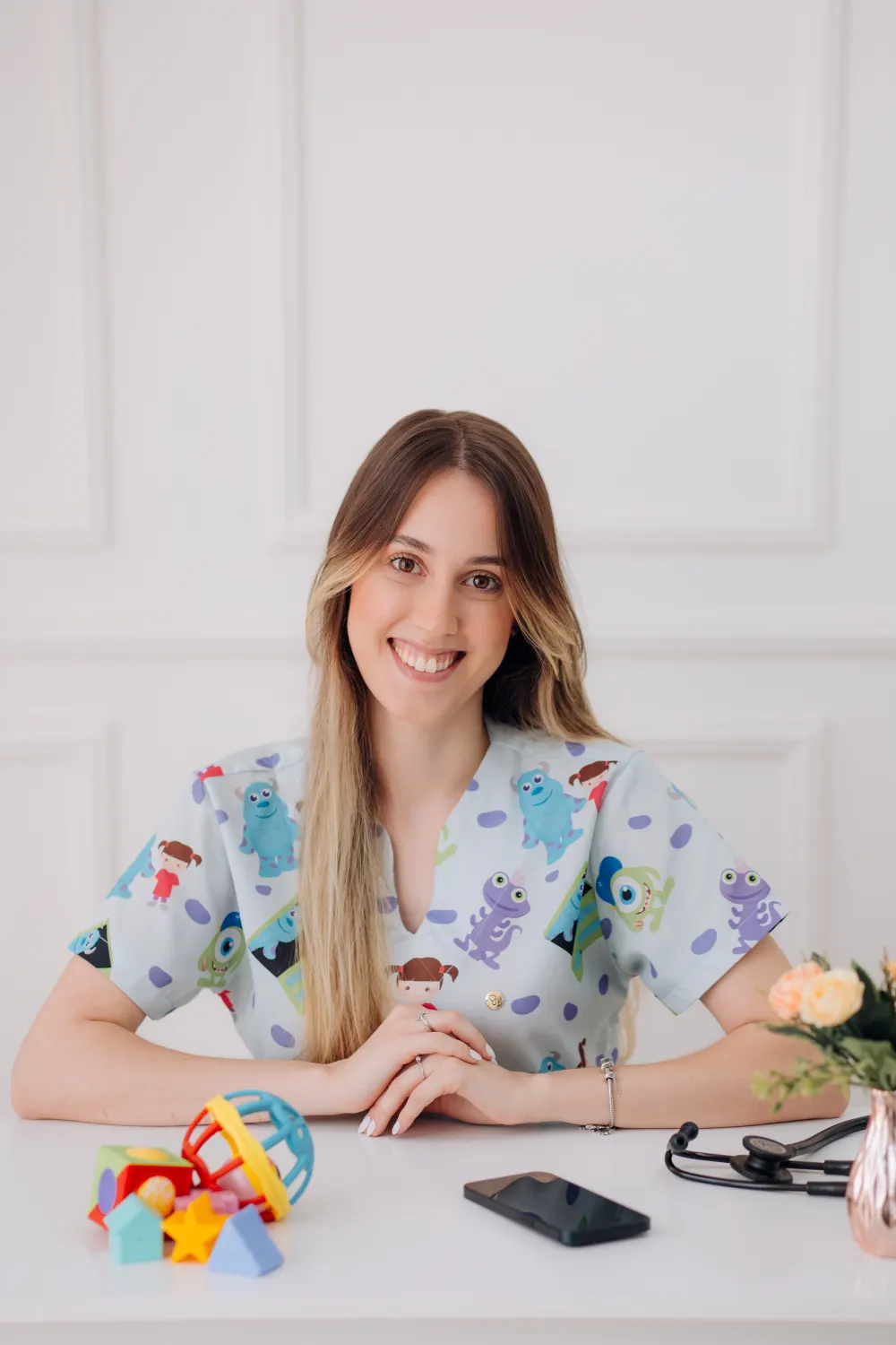 Anna Pataro, fisioterapeuta infantil, à mesa do consultório com brinquedos e estetoscópio