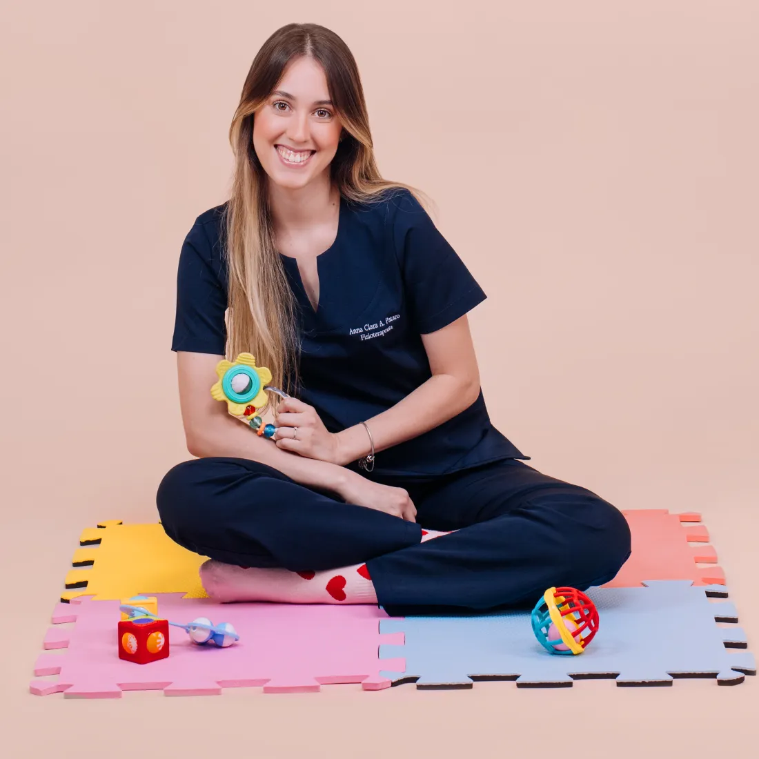 Anna Clara Pataro, fisioterapeuta infantil em Belo Horizonte, sentada no tapete de atividades com brinquedos