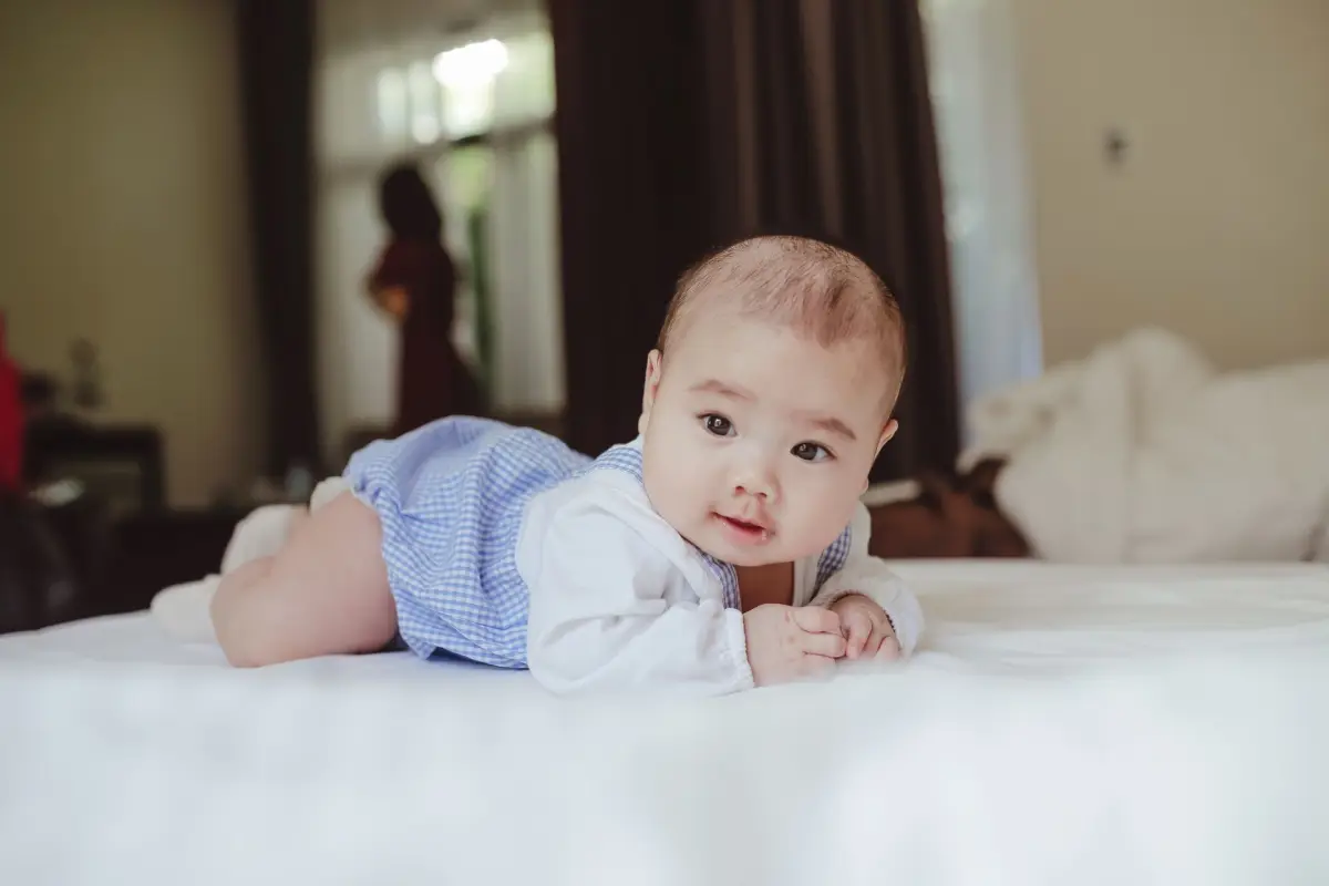 Tummy time: bebê de bruços na cama, levantando a cabeça e sorrindo